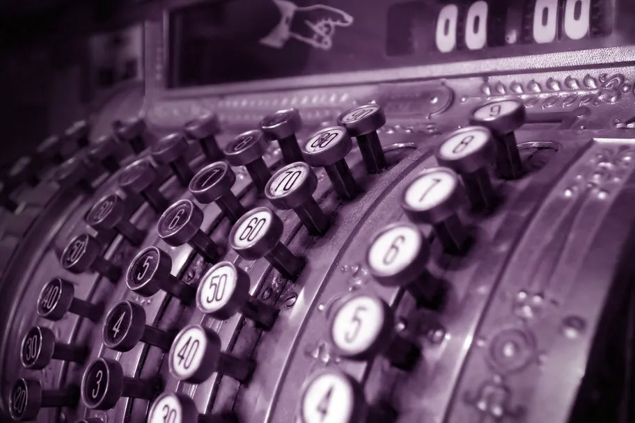 Black and white photo tinted purple of the buttons of an antique cash register.