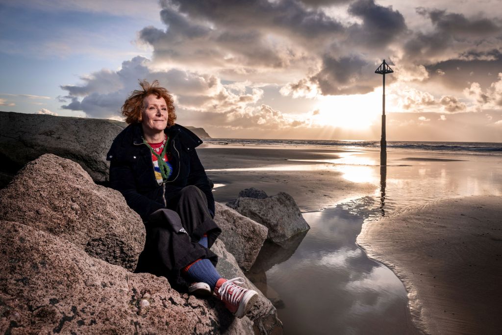 Image of Line Stockford seated upon rocks on a coastline with a contented expression.